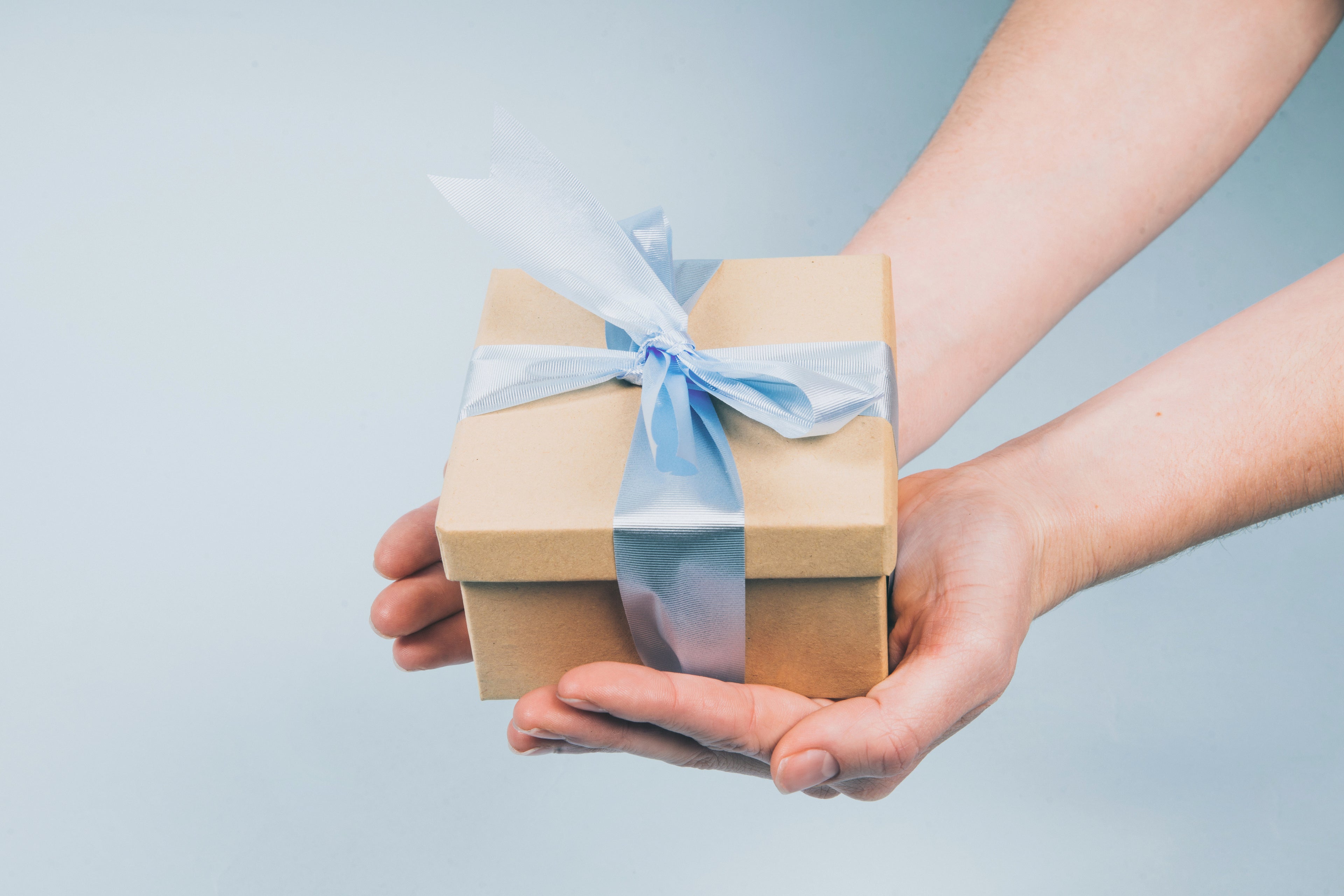 Hands holding a small gift wrapped in brown paper with a blue ribbon – MS RUKAB Global Resources Self-Care & Wellness